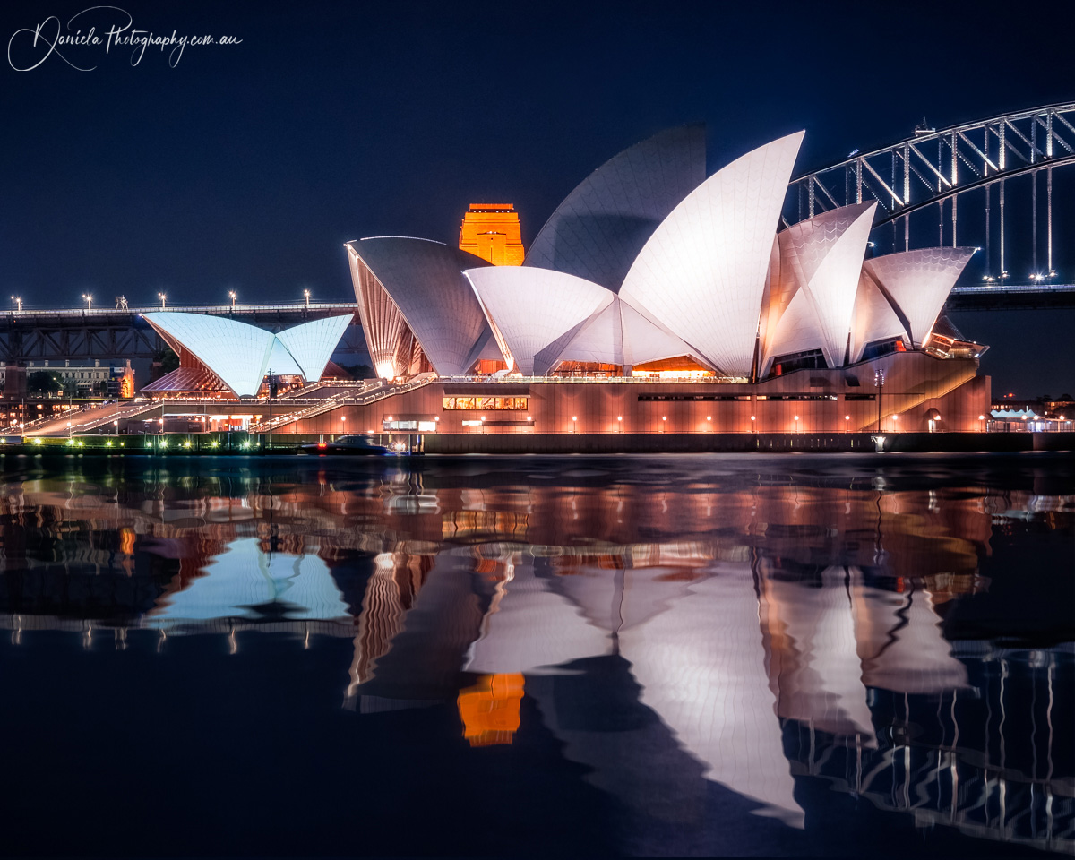 Iconic Opera House in Sydney with the white shell roofs  at Night with reflections in the water 